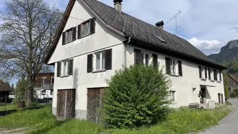 Charmantes Landhaus mit traditioneller Architektur, grüner Umgebung und Bergblick im Hintergrund.