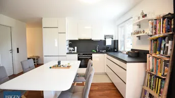 Moderne Küche mit weißen Hochglanzfronten, dunkler Arbeitsplatte und integriertem Essbereich.