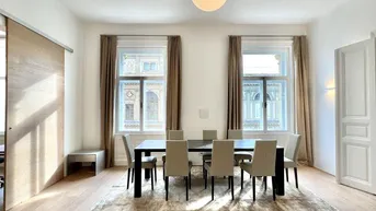 Heller Essbereich mit Holzboden, großem Esstisch und Blick auf die historische Architektur.