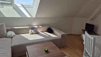 Helles Dachgeschosszimmer mit gemütlichem Sofa, Holzboden und schrägen Decken mit Dachfenstern.