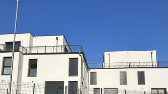 Moderne weiße Gebäude mit Flachdächern und Balkonen unter klarem blauem Himmel.