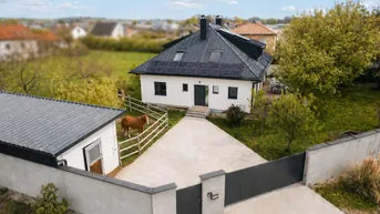 Luftaufnahme eines modernen Einfamilienhauses mit Solaranlage, großem Grundstück und Pferd auf der Weide.