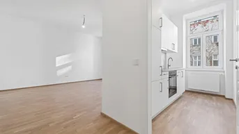 Heller Wohnbereich mit Eichenparkett und integrierter, kompakter Küchenzeile am Fenster.