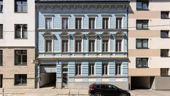Historische Fassade eines Gebäudes in hellem Blau mit vielen Fenstern und einem geparkten Auto davor.