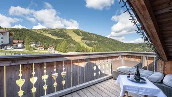 Balkon mit Holzboden, Sitzgelegenheiten und weitem Blick auf die umliegende Berglandschaft.