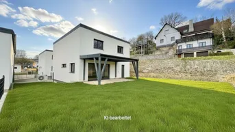 Rückseite des modernen Hauses mit grünem Rasen und überdachter Terrasse.