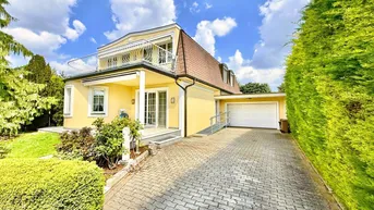 Gelbe Villa mit Mansarddach, gepflasterter Auffahrt und integrierter Garage.