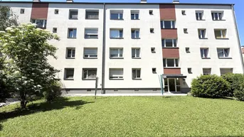 Mehrfamilienhaus mit weißer Fassade, vielen Fenstern und gepflegter Grünfläche.