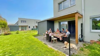 Gemütliche Terrasse mit Esstisch, Sitzgelegenheiten und Rasenfläche, ideal für Familienessen im Freien.