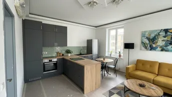 Moderne offene Küche mit Wohnbereich, grauen Schränken, Holzakzenten und einem gelben Sofa.