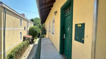 Langer Außenflur mit gelber Fassade und grüner Tür, der zu den Wohneinheiten führt.
