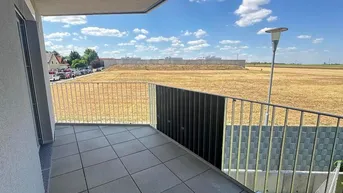 Balkon mit Fliesenboden und Blick auf ein weites Feld unter blauem Himmel.