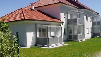 Außenansicht eines Wohnhauses mit rotem Ziegeldach, weißer Fassade und verglasten Balkonen.