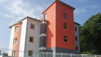 Modernes Gebäude mit auffälliger orangefarbener Fassade und runden Fenstern unter blauem Himmel.