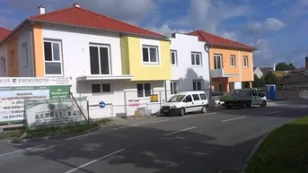 Neue Wohngebäude mit farbigen Fassaden und roten Dächern entlang einer Straße, teilweise noch im Bau.