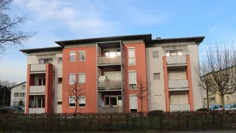 Modernes Mehrfamilienhaus mit farbiger Fassade, Balkonen und Rollläden an einem sonnigen Tag.