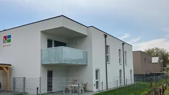 Modernes Mehrfamilienhaus mit weißer Fassade, Balkon, Terrasse und Blick auf einen Weinberg.
