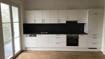 Moderne Einbauküche in Weiß mit dunkler Arbeitsplatte und Zugang zum Balkon.