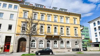 Gelbe Fassade eines historischen Gebäudes mit dekorativen Elementen und Balkon an einer Straße.