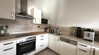 Funktionale Küche mit weißen Schränken, Holz-Arbeitsplatten und modernen Geräten unter einer Dachschräge.
