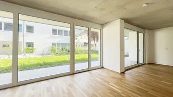 Heller Wohnraum mit großen Fenstern, Holzboden und Blick ins Grüne.