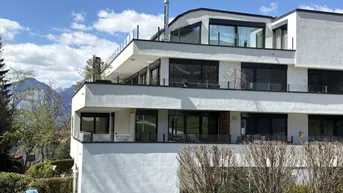 Moderne Wohnanlage mit mehreren Balkonen und Terrassen, umgeben von grüner Landschaft und Bergen.