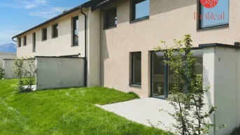 Moderne Reihenhäuser mit gepflegtem Garten, Terrasse und Bergblick unter blauem Himmel.