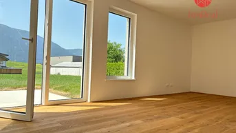 Heller Raum mit Holzboden, großen Fenstern und Bergblick, ideal für ein Wohnzimmer in einem Neubau.