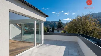 Große Dachterrasse mit hellen Fliesen, Bergblick und Zugang zu einem lichtdurchfluteten Innenraum.