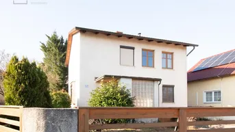 Vorderansicht eines Einfamilienhauses mit weißer Fassade und Holzzaun im Vorgrund.