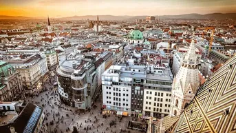 Panoramablick über eine historische europäische Stadt mit belebten Plätzen und beeindruckender Architektur im warmen Abendlicht.