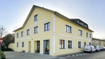 Gelbes Geschäftsgebäude mit moderner Architektur, vielen Fenstern und Parkplätzen an der Straße.