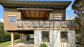 Hausfassade mit Holzverkleidung und einem möblierten Balkon im Obergeschoss.