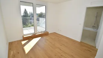 Helles Schlafzimmer mit Holzboden, Zugang zum Balkon und angrenzendem Badezimmer in einem Neubau.