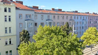 Weitblick auf eine belebte Stadtstraße mit Bäumen, Straßenbahnschienen und umliegenden Gebäuden.