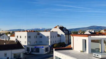 Weitblick über die Stadt mit Gebäuden, Bergen im Hintergrund und klarem Himmel.