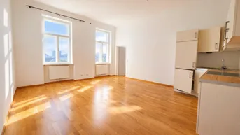 Heller Wohn- und Essbereich mit Holzboden und integrierter Küchenzeile, durchflutet von natürlichem Licht.