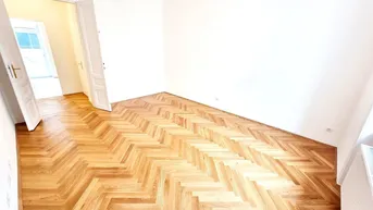 Helles Zimmer mit Fischgrätparkettboden und weißen Wänden, bereit zur individuellen Gestaltung.