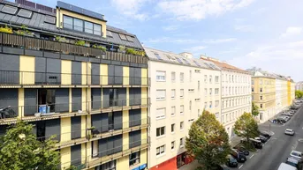 Luftaufnahme einer belebten Straße mit mehrstöckigen Gebäuden und parkenden Autos.
