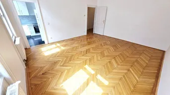 Helles Zimmer mit Fischgrätparkettboden und Zugang zu einem weiteren Raum.