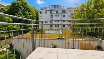 Sonniger Balkon mit Fliesenboden und Blick auf begrünte Dächer und umliegende Gebäude.