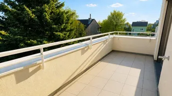 Geräumiger, sonniger Balkon mit Fliesenboden und weitem Blick ins Grüne unter blauem Himmel.
