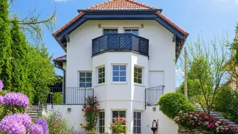 Charmantes Einfamilienhaus mit gepflegtem Garten, Rasenfläche und blühenden Pflanzen unter blauem Himmel.