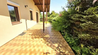 Überdachte Terrasse mit hellbraunen Fliesen und Blick ins Grüne, ideal für entspannte Stunden im Freien.