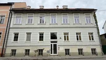Historische Fassade eines Mehrfamilienhauses mit vielen Fenstern und klassischer Architektur.