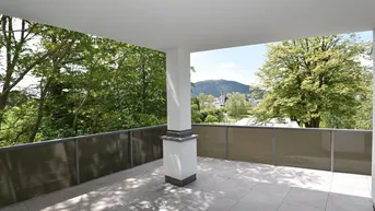 Überdachte Terrasse mit Fliesenboden und weitem Blick auf die grüne Landschaft und Berge.