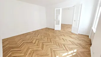 Helles Zimmer mit Fischgrätparkett, hohen Decken und Stuckelementen, bereit zur individuellen Gestaltung.