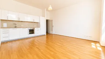 Helles Wohnzimmer mit integrierter Küche, Parkettboden und weißen Schränken.