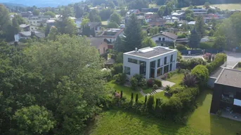 Luftaufnahme des modernen Hauses mit Flachdach, umgeben von viel Grün und einer Wohnsiedlung.