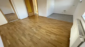 Heller Raum mit Holzboden und Heizkörper, der vielseitig nutzbar ist und auf einen weiteren Raum blickt.